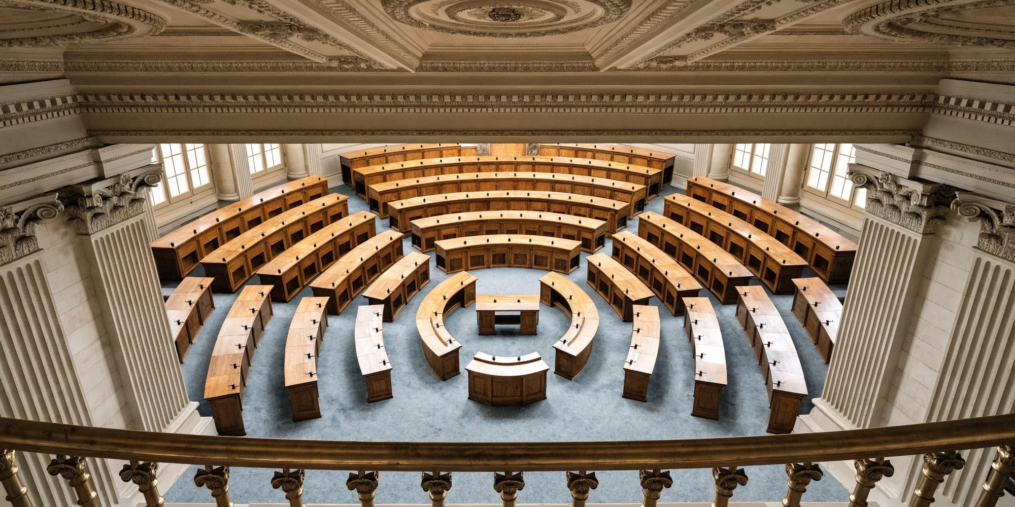 An empty upper-chamber legislative room seen from the visitors' gallery, with concentric semicircular rows of desks