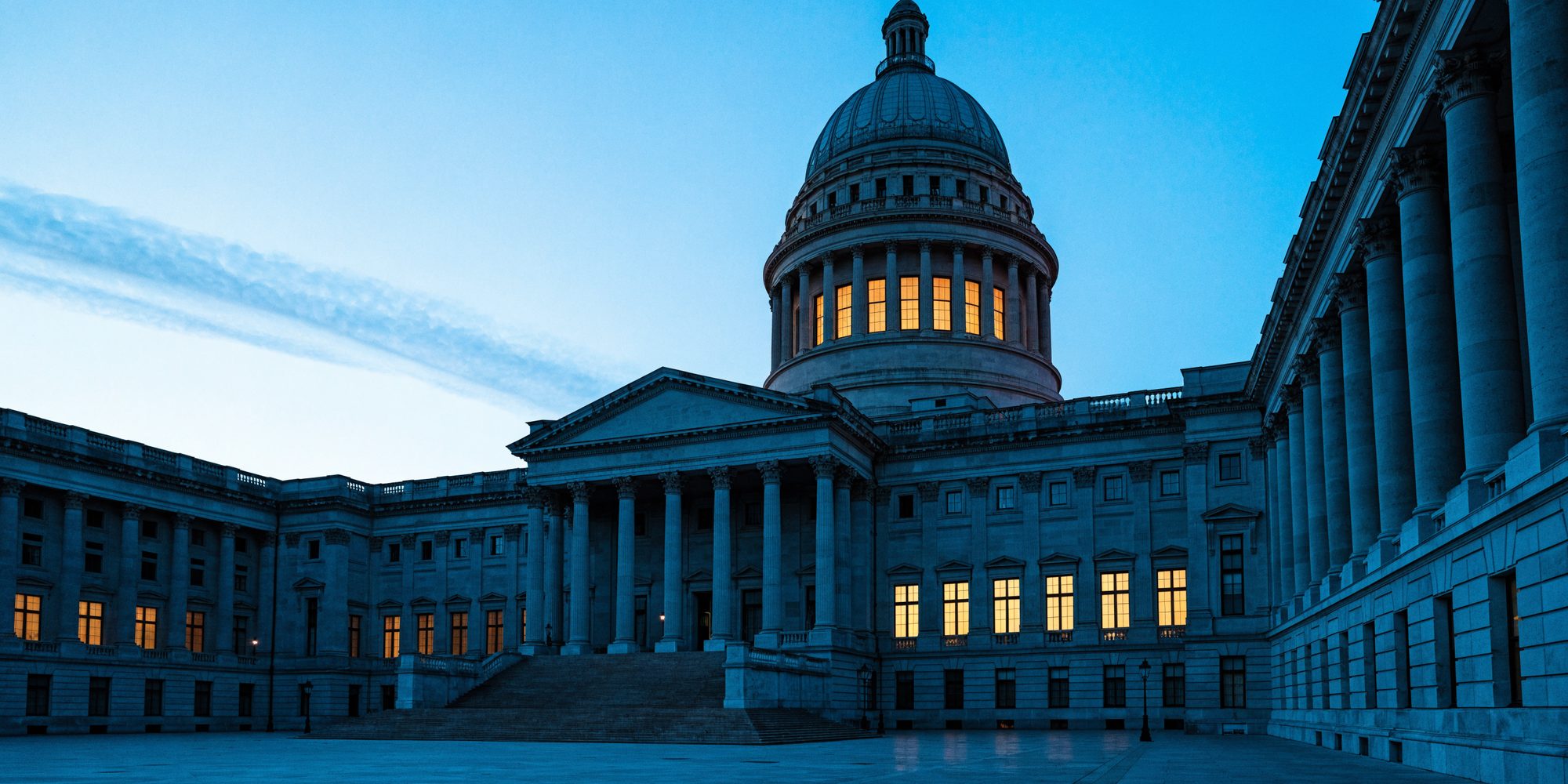 A domed neoclassical capitol building photographed at dusk, its windows lit from within
